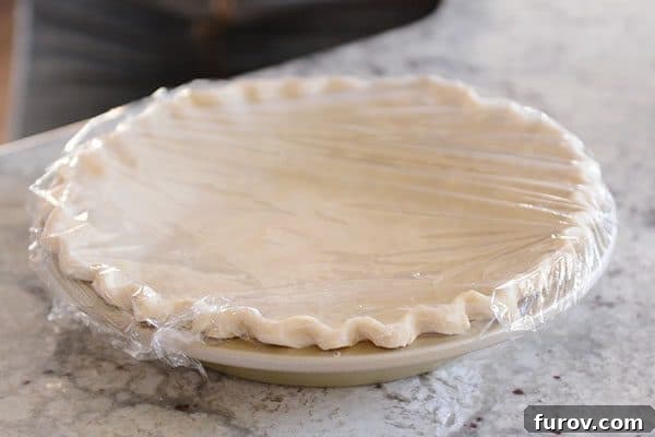 An uncooked pie crust with a crimped edge, covered in saran wrap.