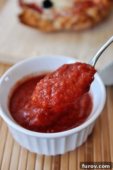 A spoonful of pizza sauce being taken out of a ramekin of pizza sauce.