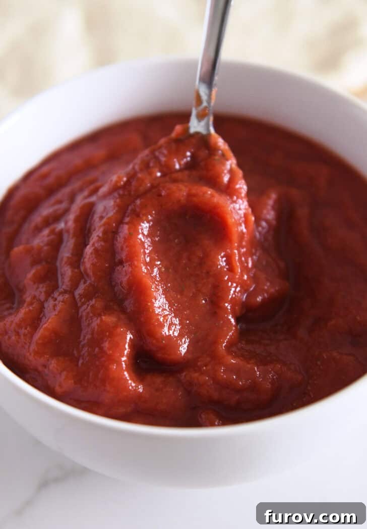 Metal spoon stirring pizza sauce in a white bowl.