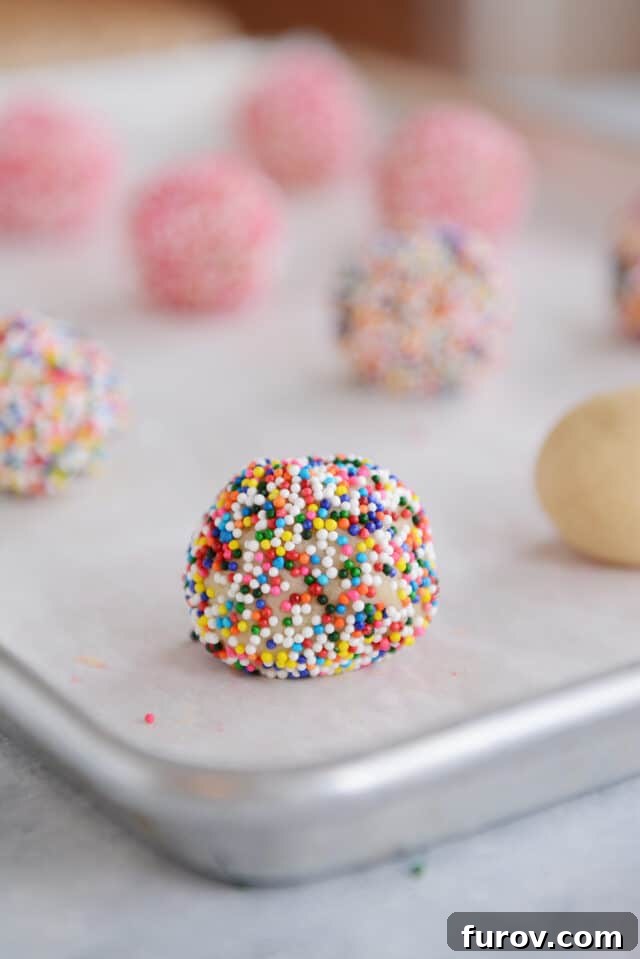 Effortless Soft and Chewy Drop Sugar Cookies 5 Cookie dough ball thoroughly rolled in sprinkles, placed on a baking sheet ready for the oven.