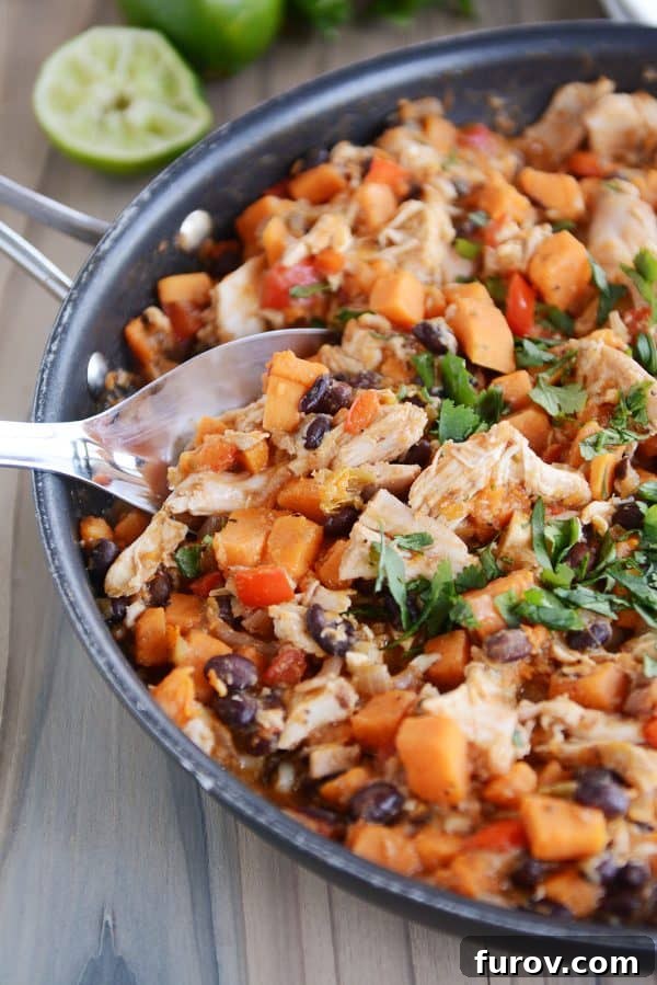 A spoon lifting a hearty scoop of cheesy Mexican chicken and sweet potato mixture from the skillet, showcasing melted cheese and vibrant ingredients.