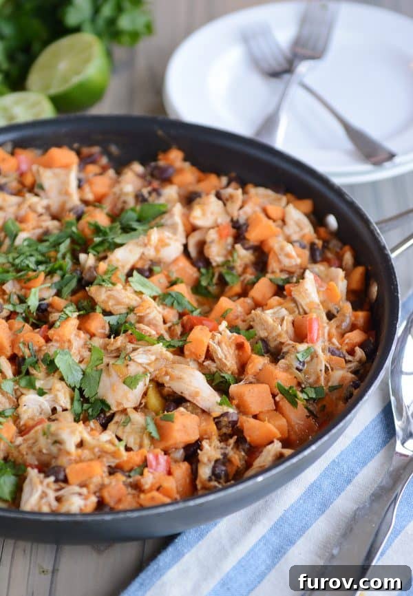 A close-up of a skillet filled with the cheesy Mexican chicken and black bean mixture, showing the melted cheese bubbling over the rich ingredients.