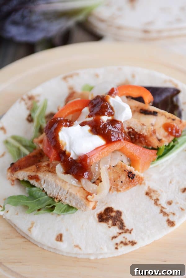 A vibrant grilled chipotle chicken wrap, generously filled with tender chicken, sour cream, colorful bell peppers, and fresh salsa, ready to be enjoyed.