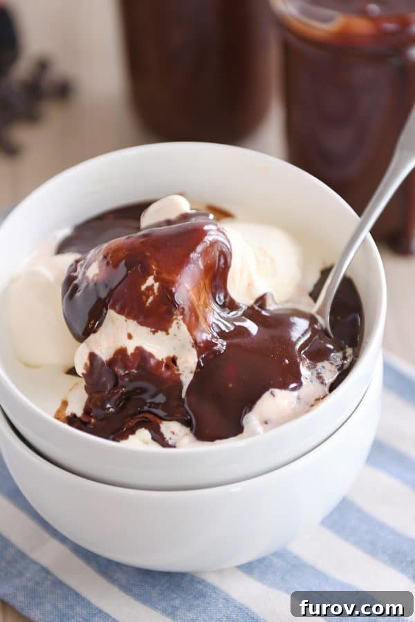 Creamy vanilla ice cream in a white bowl, generously topped with glistening, rich 5-minute hot fudge sauce, ready to be enjoyed as a delightful dessert.
