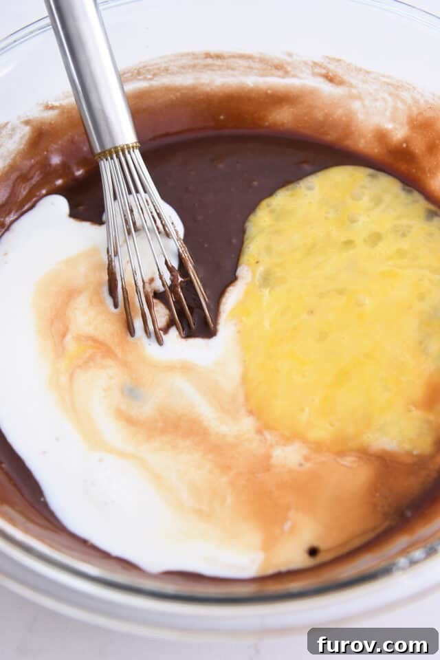 Adding buttermilk and eggs to chocolate cake batter. Incorporating the final liquid ingredients for a smooth batter.