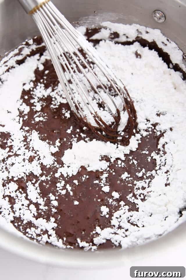 Whisking powdered sugar into melted cocoa and butter in saucepan. Achieving a smooth, lump-free frosting consistency.