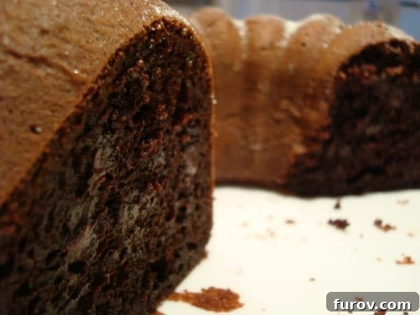 A whole chocolate bundt cake with a slice taken out, sitting on a white plate, ready to be enjoyed.