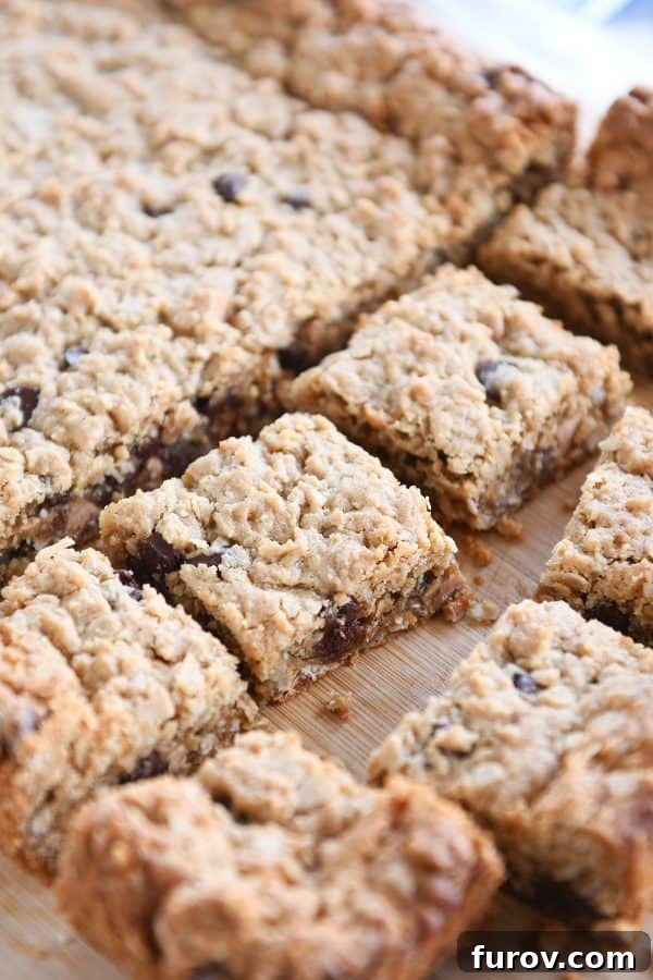 A generous slab of freshly baked butterscotch peanut butter monster cookie bars, perfectly cut into squares and arranged on a rustic wooden board, showcasing their inviting texture and colorful chips.