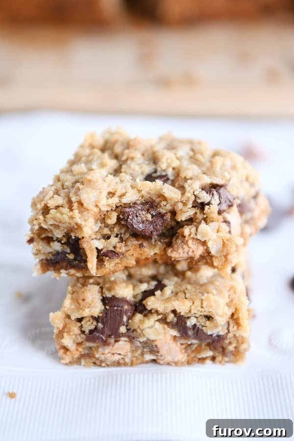 Two soft and chewy butterscotch peanut butter monster cookie bars, one with a bite taken out, stacked against each other, revealing their oatmeal texture and melty chips.