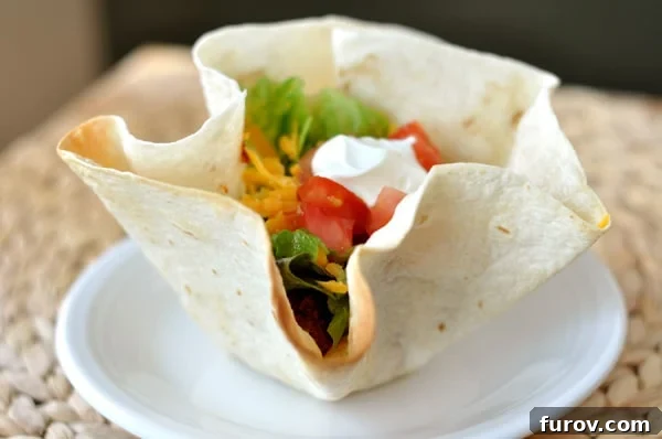 A perfectly baked tortilla bowl brimming with seasoned taco meat, shredded lettuce, diced tomatoes, and a dollop of sour cream.
