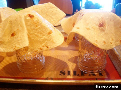 Six flour tortillas carefully draped over inverted mason jars on a baking sheet, ready for baking.