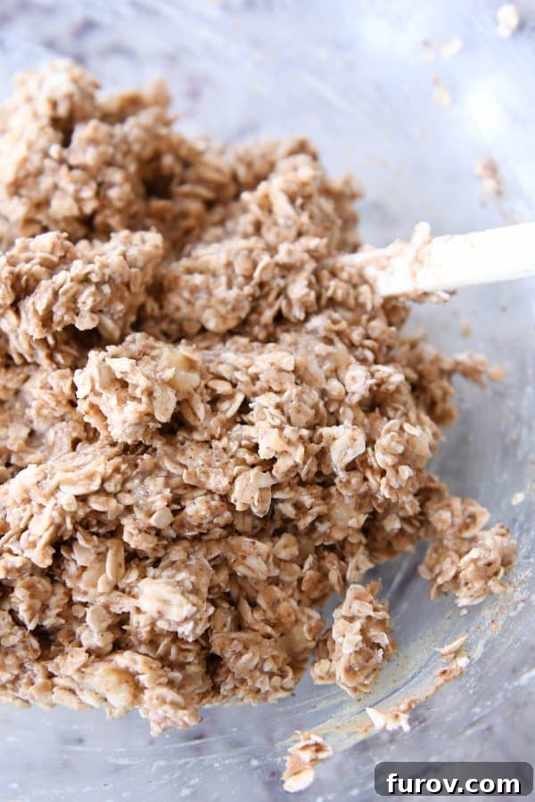 Raw oat cookie dough in a clear glass bowl, showcasing the rich texture before baking.