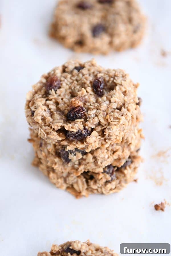 A neatly stacked pile of cooked oatmeal raisin breakfast cookies, resting on a piece of parchment paper.