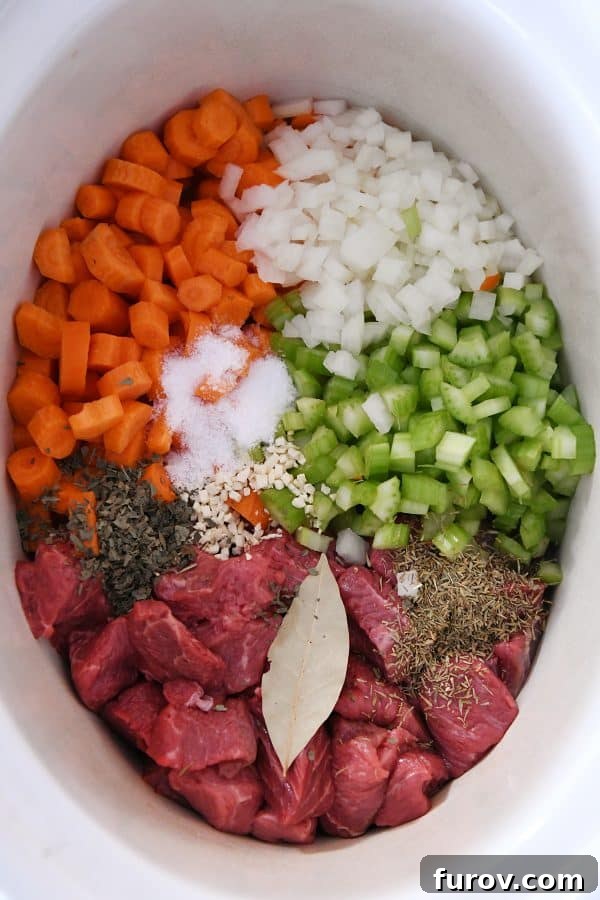 Top down view of beef, veggies, and seasonings in slow cooker.