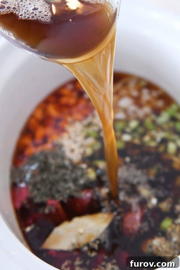 Adding beef broth to slow cooker for beef vegetable noodle soup.