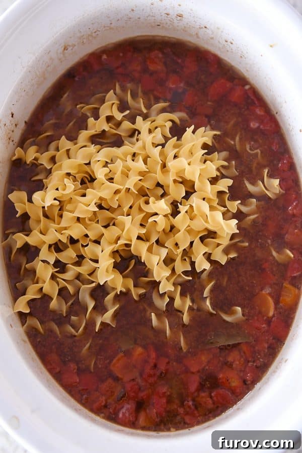 Adding dry egg noodles to slow cooker for beef noodle soup.
