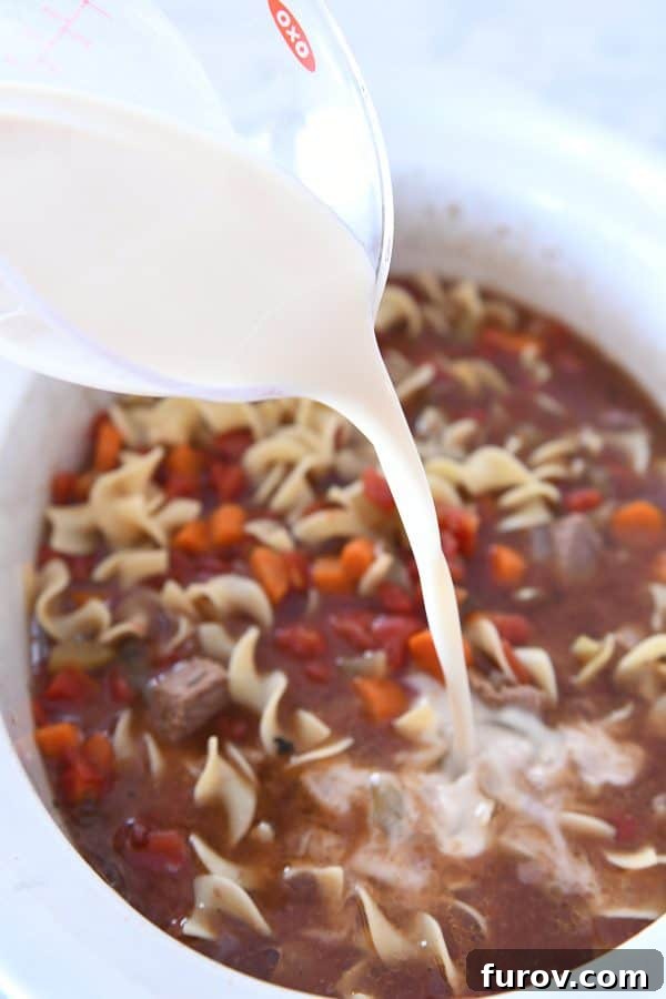 Adding cornstarch slurry to slow cooker for beef vegetable noodle soup.