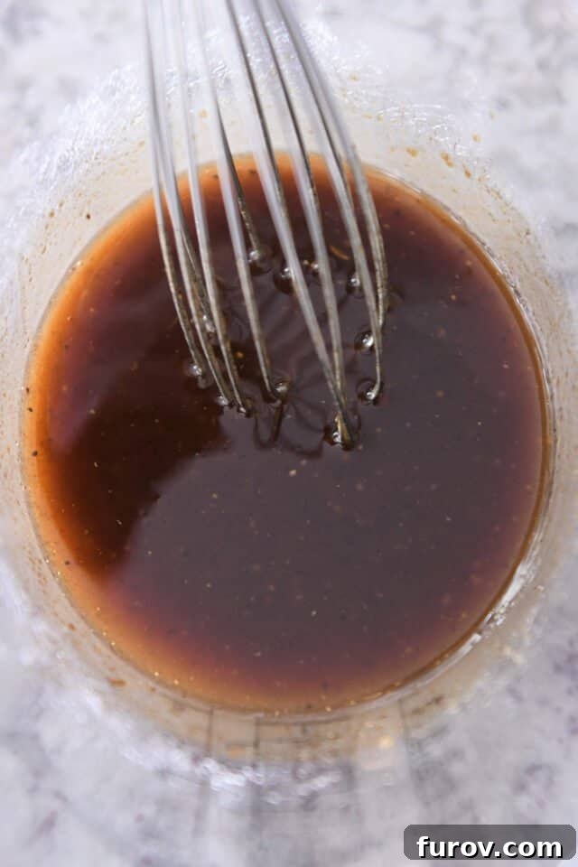 Mouthwatering Grilled Pork Chops 3 A liquid measuring cup filled with the golden-brown marinade, with a whisk resting inside, showcasing its rich consistency and inviting aroma.