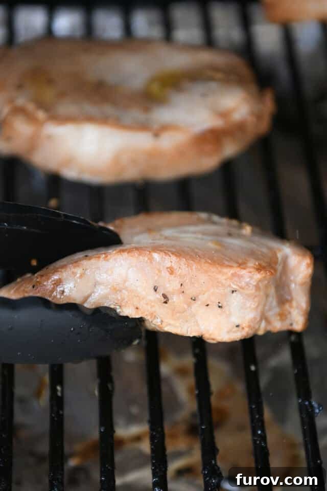Mouthwatering Grilled Pork Chops 5 A pair of stainless steel tongs carefully flipping a sizzling pork chop on a hot grill, showing perfect sear marks and a juicy texture.