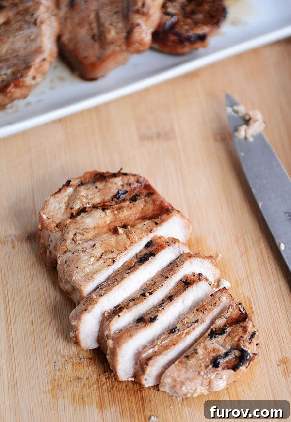 Mouthwatering Grilled Pork Chops 6 A perfectly grilled pork chop, expertly sliced against the grain on a rustic wooden cutting board, revealing its incredibly juicy, tender interior.