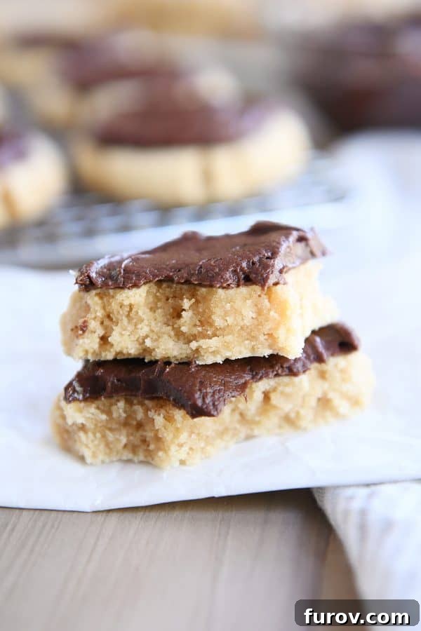A stack of soft peanut butter sugar cookies, one broken in half to reveal its tender interior, all topped with luscious chocolate frosting.