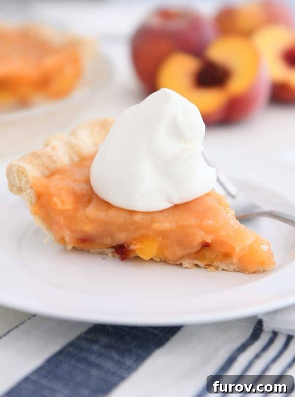Slice of fresh peach pie on white plate with spoonful of whipped cream on top.