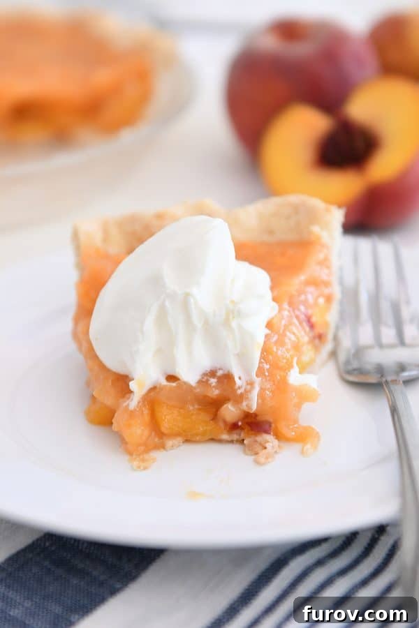 Slice of fresh peach pie on white plate with bite taken out.