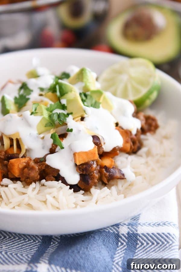White rice topped with a vibrant medley of sweet potato, black beans, seasoned ground beef, sliced avocados, fresh cilantro, and lime wedges, creating an enticing skillet burrito bowl.