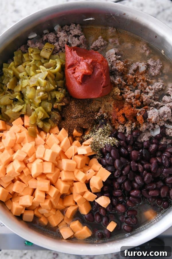 A vibrant close-up of a skillet filled with the simmering sweet potato, black bean, and seasoned ground beef mixture, along with green chiles, and tomato paste, ready to cook.