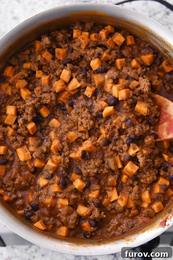 A wooden spoon poised in a skillet, showcasing the perfectly cooked and tender sweet potato and black bean burrito filling, ready for serving.