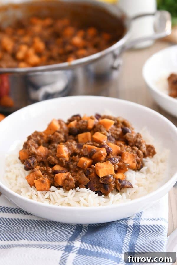 A white bowl holds a generous serving of rice, beautifully topped with the warm and savory sweet potato and black bean burrito filling.