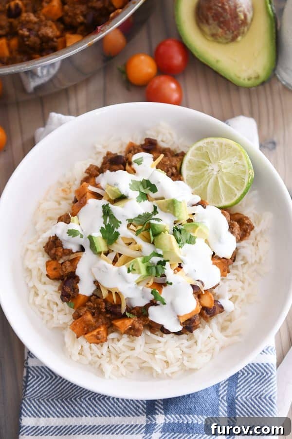 A stunning top-down view of a completed sweet potato black bean burrito bowl, featuring white rice, the flavorful skillet mixture, vibrant avocados, fresh cilantro, and bright lime wedges.
