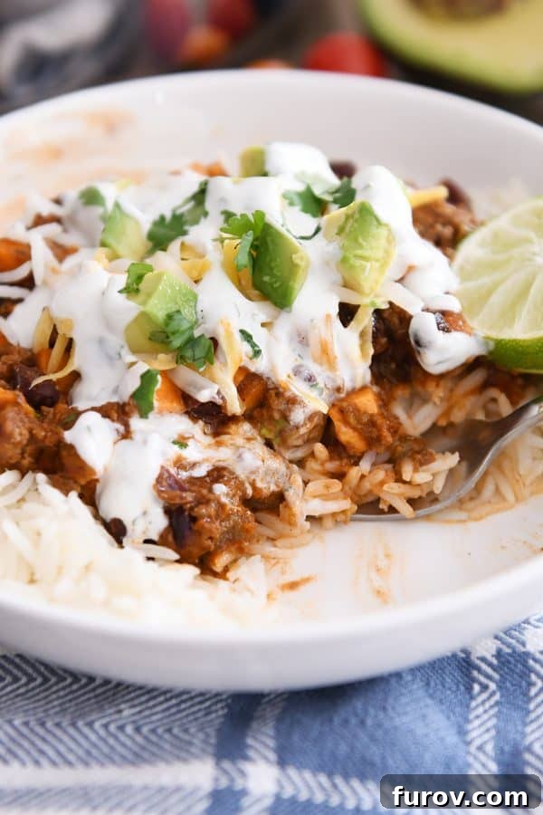 A person is scooping a flavorful bite from a white bowl filled with sweet potato black bean burrito bowl ingredients, showcasing the meal's delicious appeal.