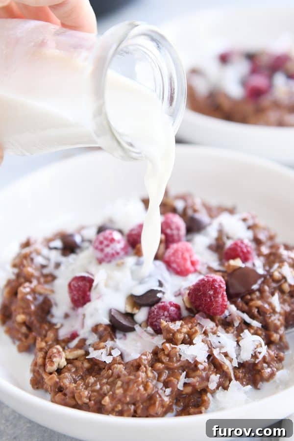 Rich & Dreamy Instant Pot Double Chocolate Steel Cut Oats 2 Pouring milk over Instant Pot chocolate steel cut oats in a white bowl with frozen raspberries.