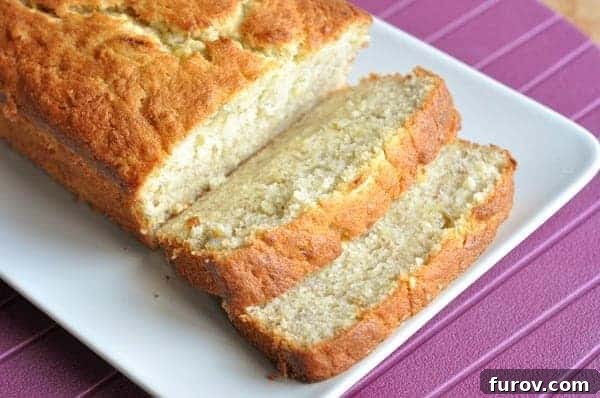 A beautifully baked loaf of buttermilk banana bread with two slices cut and placed on a white ceramic plate, ready to be served.