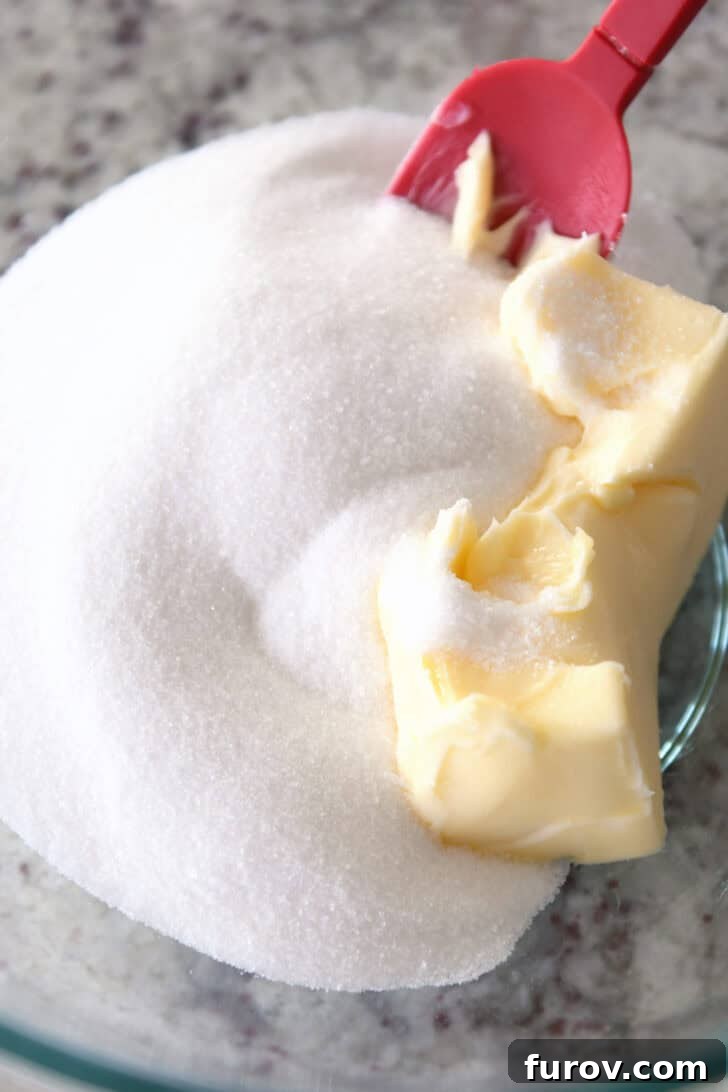 Top-down view of granulated sugar and softened butter being creamed in a glass mixing bowl.