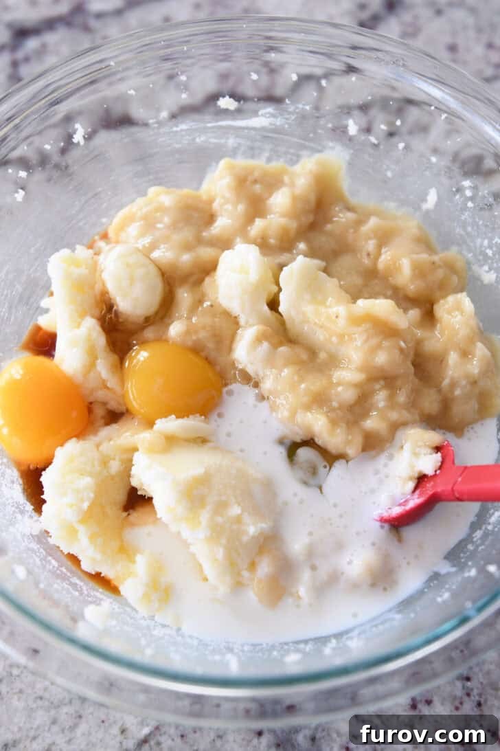 Top-down view of wet ingredients including mashed bananas, eggs, and buttermilk in a glass bowl.