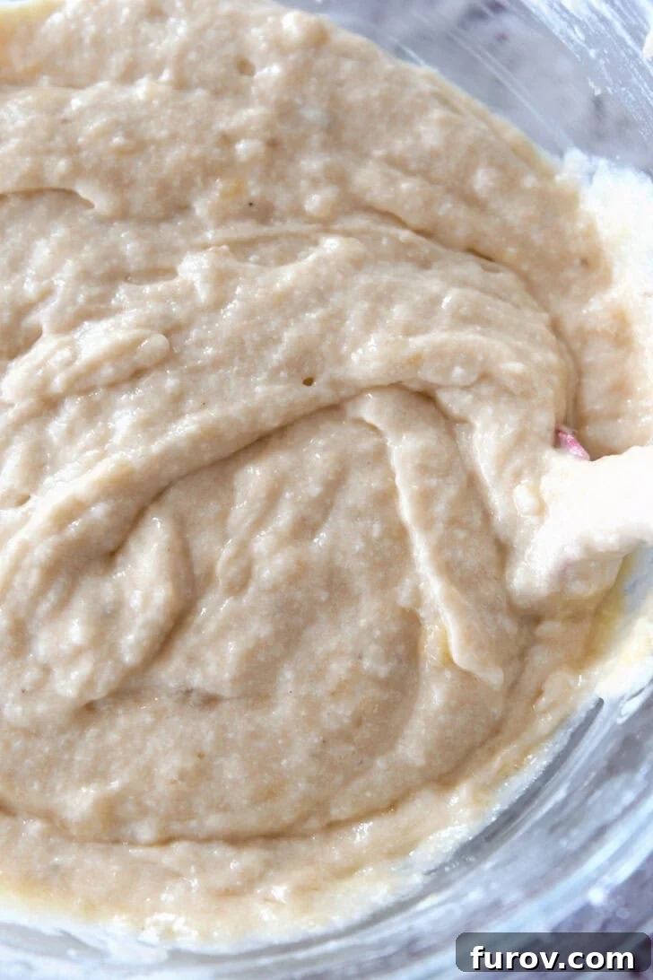 Top-down shot of smooth, golden banana bread batter being mixed gently in a glass bowl.