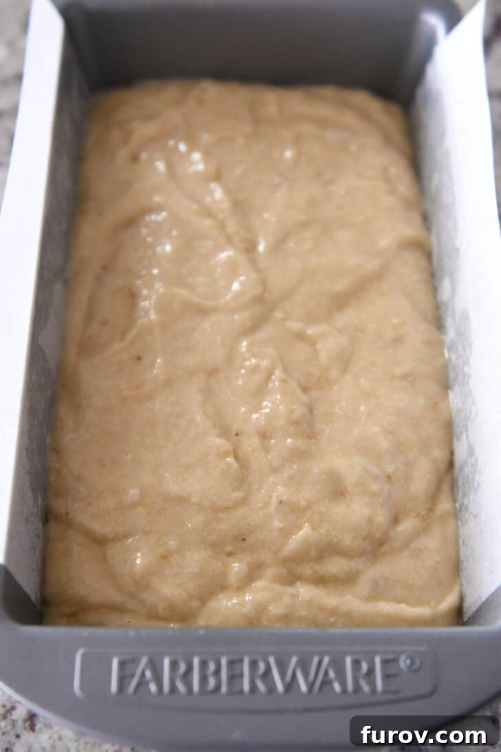 Top-down view of smooth banana bread batter neatly poured into a greased metal loaf pan, ready for baking.
