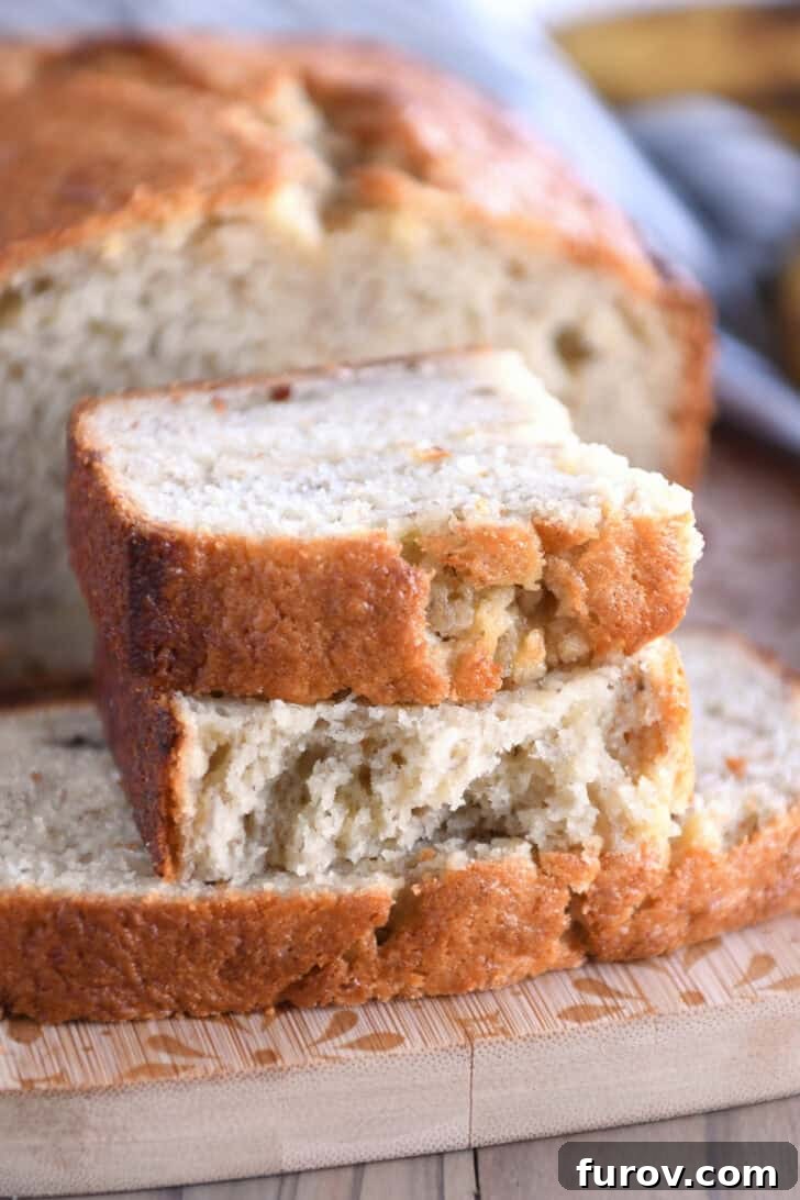 Two perfect half-slices of golden buttermilk banana bread with a soft interior on a wooden cutting board.