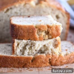 Two half slices of banana bread on wood cutting board, showcasing its fluffy texture.