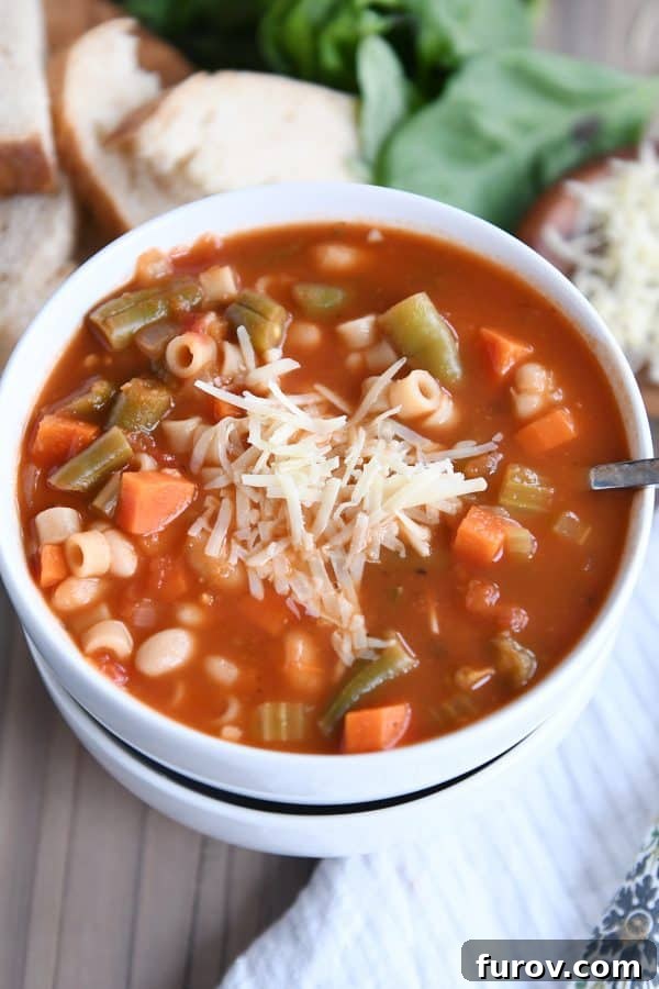 Two stacked white bowls filled with steaming minestrone soup, garnished with grated Parmesan cheese.
