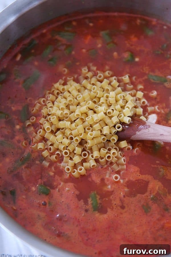 Ditalini pasta simmering in a pot with broth, tomatoes, and mixed vegetables.