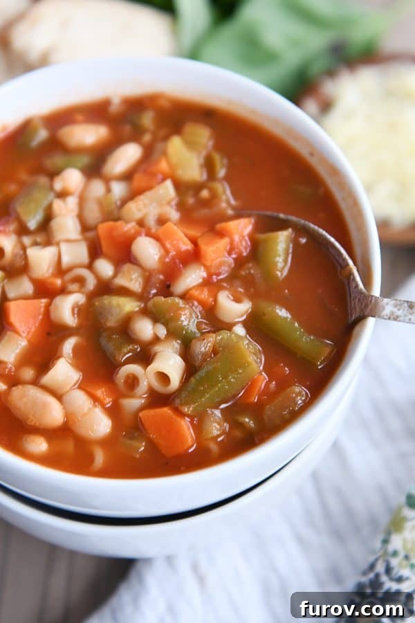A spoon resting in a bowl of classic minestrone soup, part of two stacked white bowls.