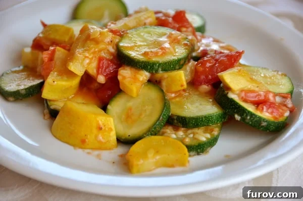 A close-up of the cooked zucchini and yellow squash, vibrant with color and glistening with olive oil, paired with fresh, juicy tomatoes on a white plate, highlighting its fresh appeal.