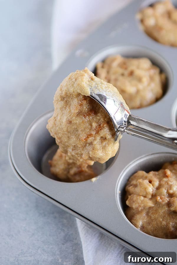 A muffin tin full of bran muffin batter, with an ice cream scoop filling the last slot in the muffin tin. 