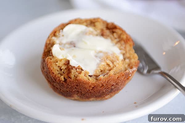 A half of a bran muffin on a white plate with butter spread on it. 