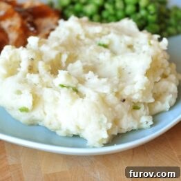 Close-up of baked garlic mashed potatoes with a crispy top, served on a white plate with a side of green peas and pork.