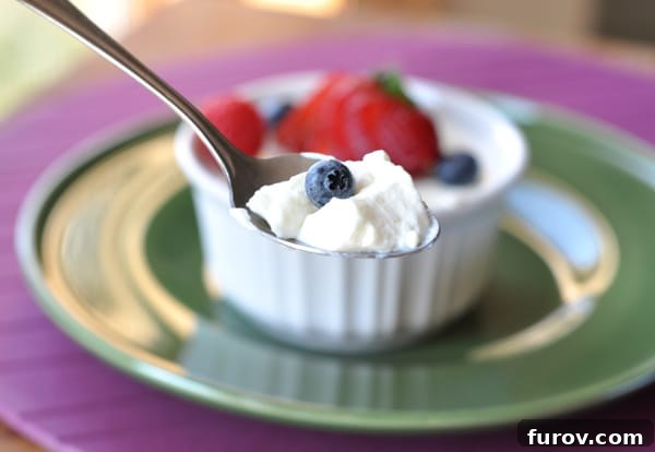 Small white ramekin with creamy dessert topped with fresh berries and a spoon taking a bite, showing the rich texture.
