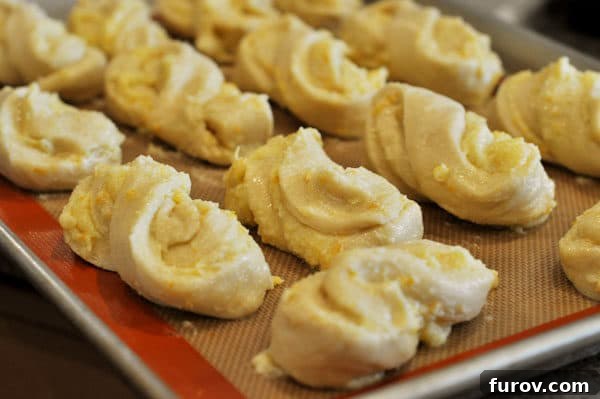 Golden Orange Swirls 11 uncooked twisted orange rolls lined up on a sheet pan, perfectly spaced for their final rise
